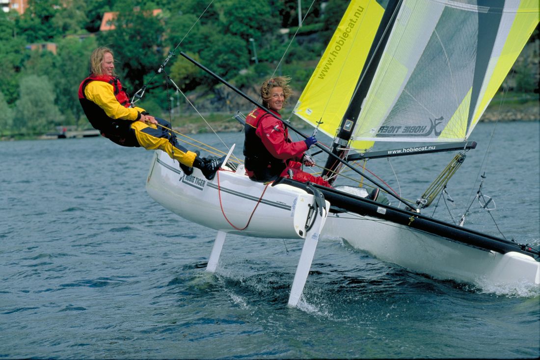 Two sailors on the trapeze of a Hobie catamaran at speed